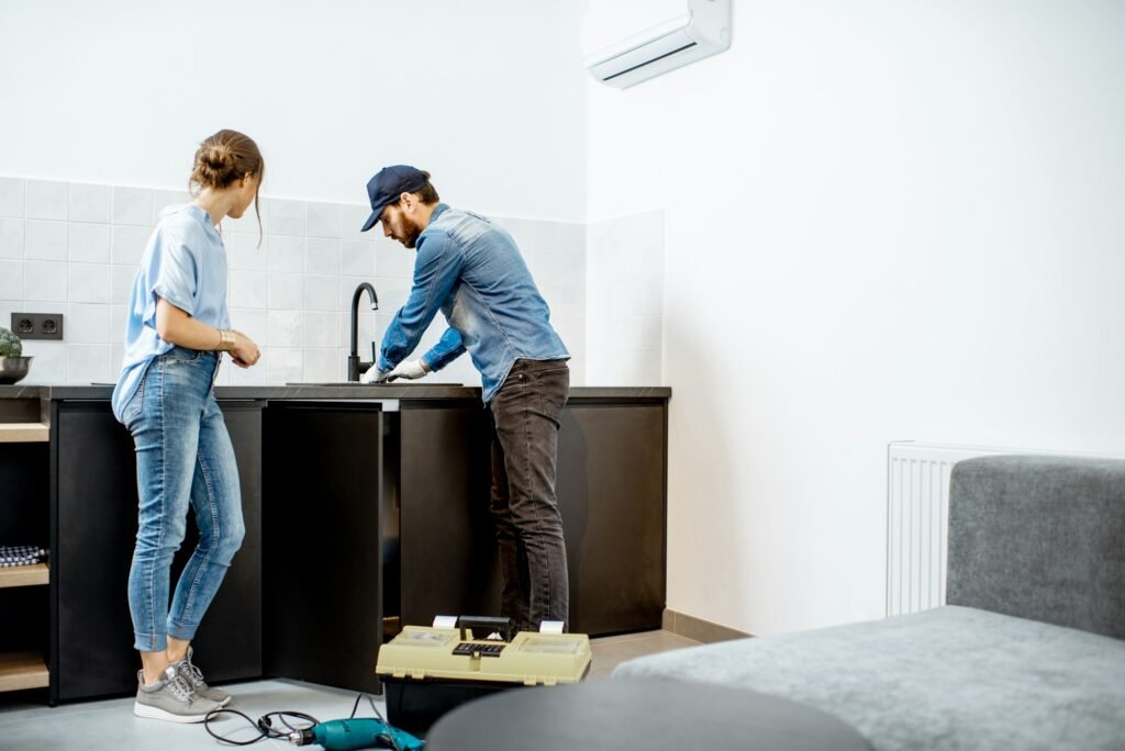 Plumber repairing kitchen faucet with woman in the apartment